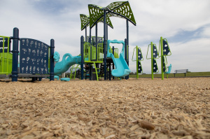 Playground at Mountain Ridge Park with slides, climbing structures, and play panels, shown from ground level with wood chips in the foreground.