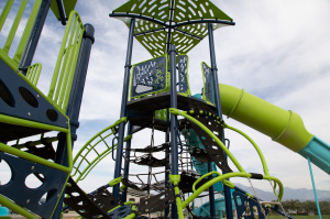 Close-up view of the playground climbing tower at Mountain Ridge Park, with rope ladders, climbing features, and a large green tube slide.
