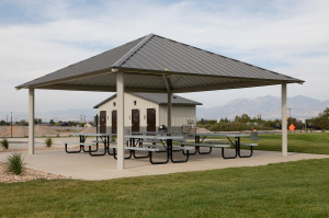 Covered pavilion with picnic tables at Mountain Ridge Park, with the restroom building in the background and mountains in the distance.