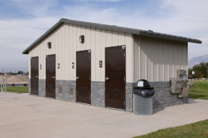 Restroom building at Mountain Ridge Park with four brown doors, water fountains, and a trash can along the sidewalk.